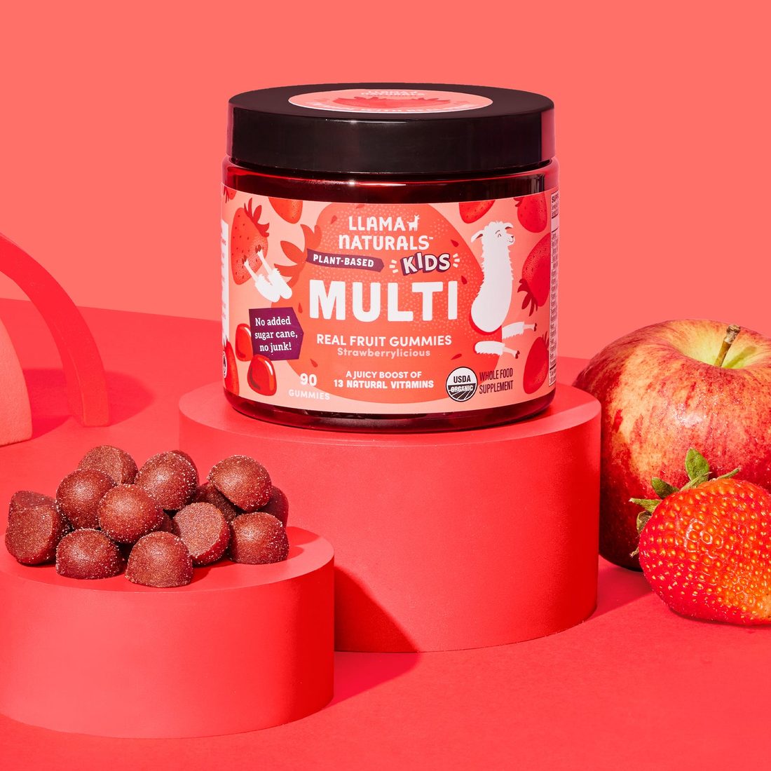 Llama Naturals Kids Multi jar surrounded by fresh strawberries, an apple, and gummies