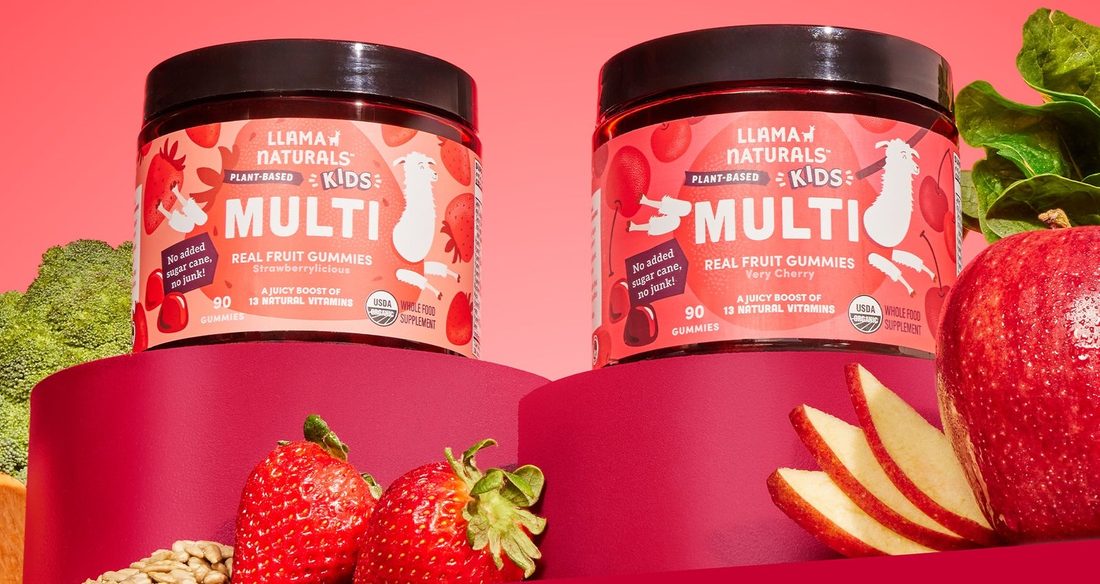 Two Llama Naturals Kids Multi jars surrounded by strawberries, apple slices, oats, and kale